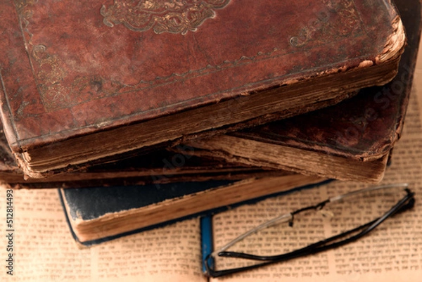 Fototapeta Old worn shabby leather-bound jewish books on open blurred Torah in the background. Closeup. Selective focus.
