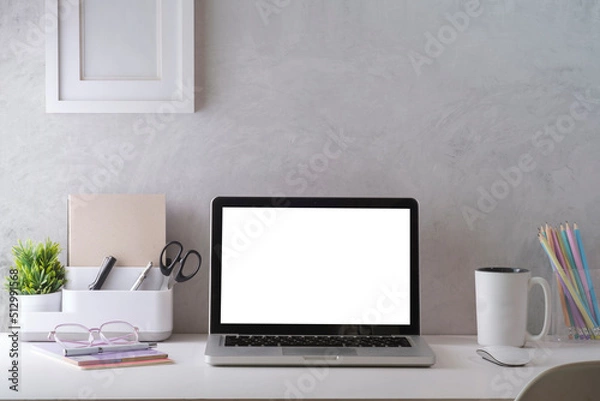 Fototapeta Mockup laptop with empty display, coffee cup, books and picture frame on white table.