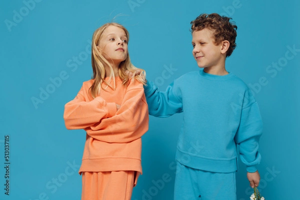 Fototapeta two children, brother and sister stand on a blue background in bright clothes and the girl is very offended by the boy. Friendship, relationship