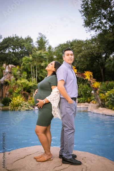Obraz husband and pregnant wife touching each other's backs near swimming pool surrounded by tropical jungle