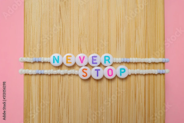 Fototapeta a beaded bracelet with the inscription never stop on a pink background with a copy space.