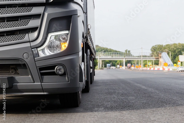 Fototapeta The concept of cargo transportation. A black truck is parked on the side of the highway.  Front view of a heavy truck. Front headlight close-up. A place to copy.