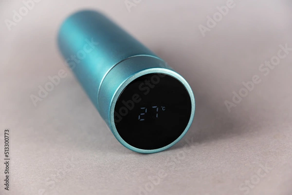 Obraz Modern thermos lies on a gray background. Black lid with LED digital display. Temperature reading 27 degrees Celsius. Cylindrical vacuum flask of turquoise color. Container for hot and cold drinks.