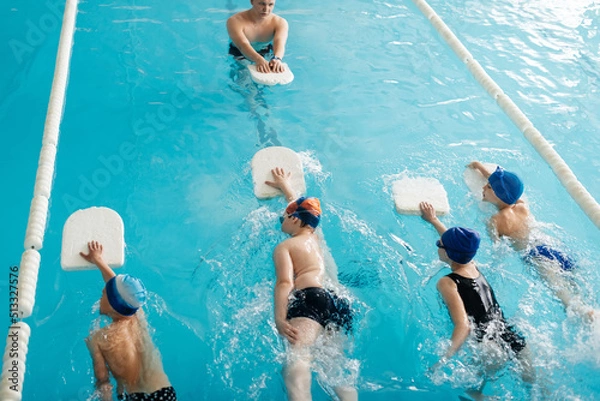 Fototapeta A group of boys and girls train and learn to swim in a modern swimming pool with an instructor. Development of children's sports. Healthy parenting and promotion of children's sports.