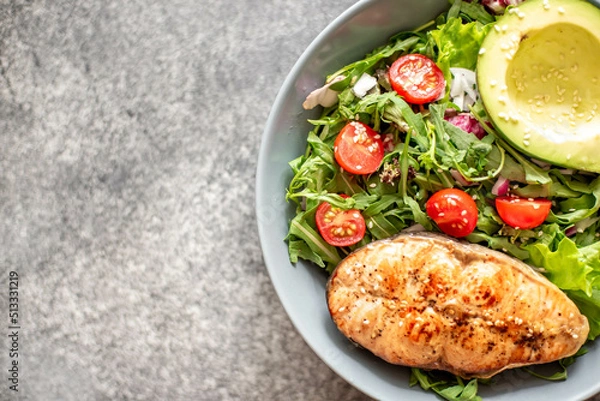 Fototapeta grilled salmon steak and fresh green vegetable tomato salad with lettuce and avocado on stone background with copy space for your text