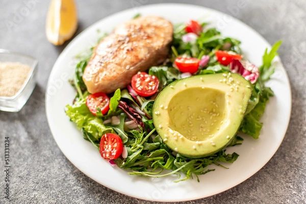 Obraz grilled salmon steak and fresh green vegetable tomato salad with lettuce and avocado on stone background