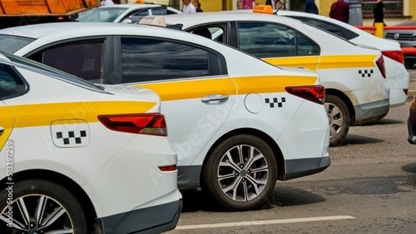 Fototapeta White and yellow taxis stand in a tight traffic jam on a hot sunny day. Synchronous arrangement of cars
