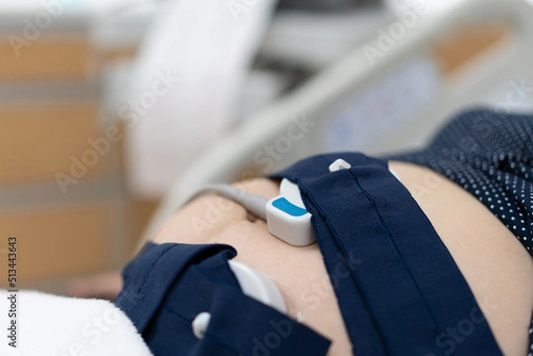 Fototapeta Pregnancy care. Fetal heartbeat monitoring by cardiotocography from electronic fetal monitor. Pregnant belly installed with belt for heartbeat examination. Pregnancy care technology concept.