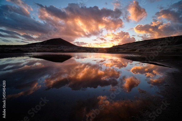 Fototapeta sunset sunrise, orange clouds, reflection of the skin on the water, with mountains in the background