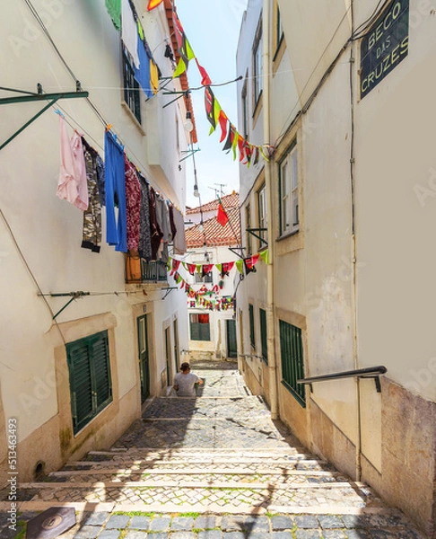 Obraz The young man sits on the steps of a staircase on a narrow old street in Alfama. Lisbon, Portugal