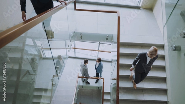 Fototapeta Top view of two businessmen meet at staircase in modern office center indoors and talking while female colleagues walking stairs