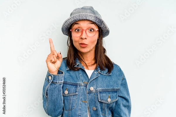 Fototapeta Young hispanic woman isolated on blue background holds copy space on a palm, keep hand over cheek. Amazed and delighted.
