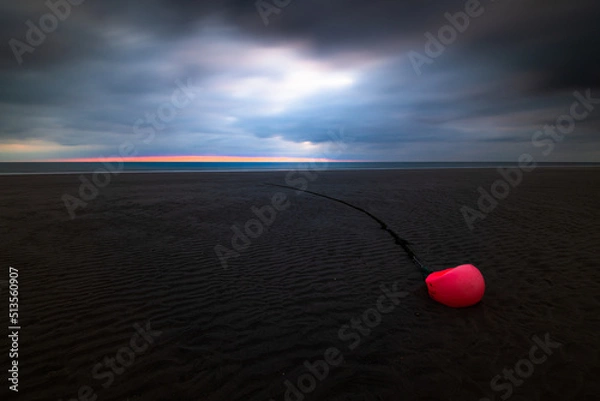 Fototapeta Orange buoy at the beach of Amrum island Germany during low tide with glowing dramatic sky and dark stormy clouds at sunset
