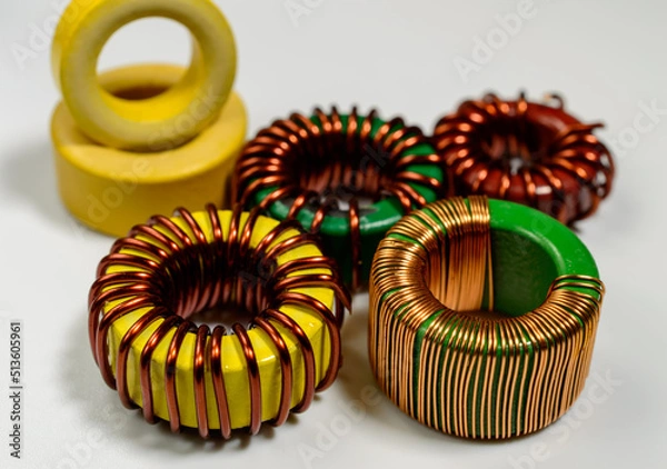 Fototapeta Small family of inductive chokes on a white background. Inductive component, copper wire coil, yellow toroid - macro picture. 