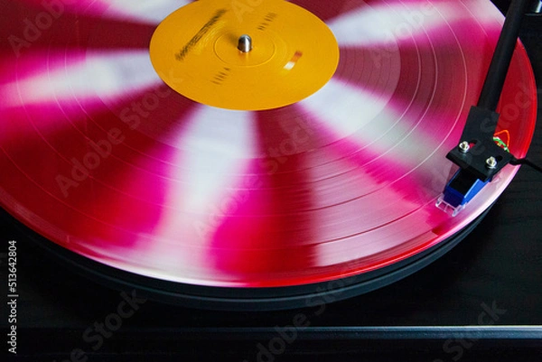 Obraz Red, Pink and white vinyl record spinning on a turntable, stylus on the record, blurred motion, in the groove