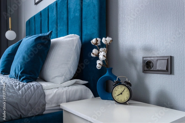 Fototapeta Analog clock alarm clock on the nightstand by the bed against the background of pillows