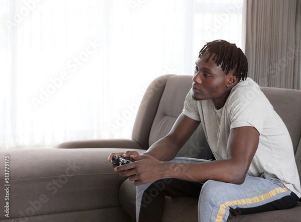 Obraz African american guy playing video game with joystick at home