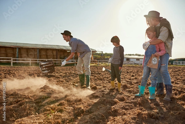 Fototapeta Family looking at father digging ground on field
