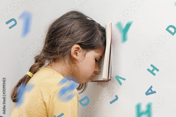 Fototapeta Sad and tired caucasian girl with dyslexia holds a book on her forehead. Flying tangled letters in the air. The child learns to speak and read correctly