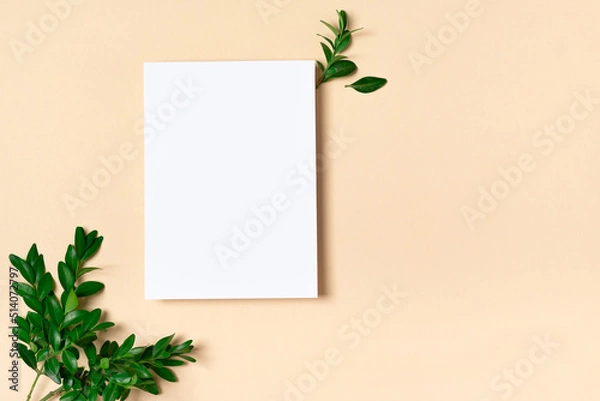 Obraz Rectangular vertical or square invitation white greeting card mockup with a boxwood branch. Top view with copy space, pastel light yellow beige background. Template for branding and advertising