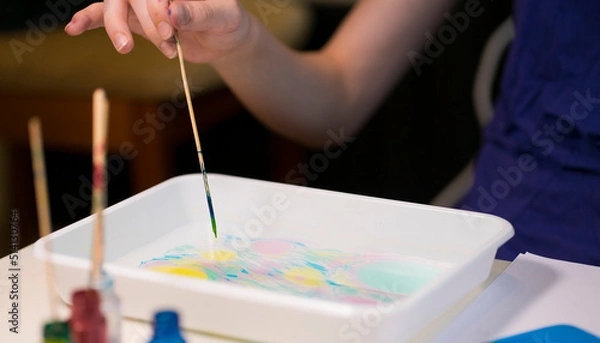 Fototapeta Girl draws with a stick on the water. Image with selective focus