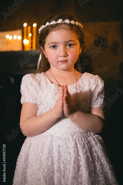 Fototapeta Little armenian redhead girl in ancient armenian monastery praying and looking at camera in front of candles