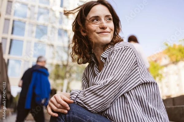 Obraz happy smiling young woman sitting in city looking to the side