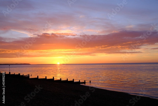 Fototapeta View of a beautifully colourful seaside sunset across a beach silhouette.