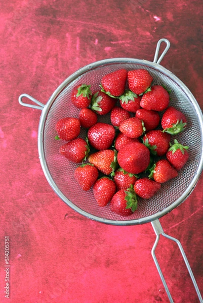 Fototapeta Juicy strawberry in a strainer. Red textured background with copy space. Simple composition still life with summer berries. Eating healthy concept. 