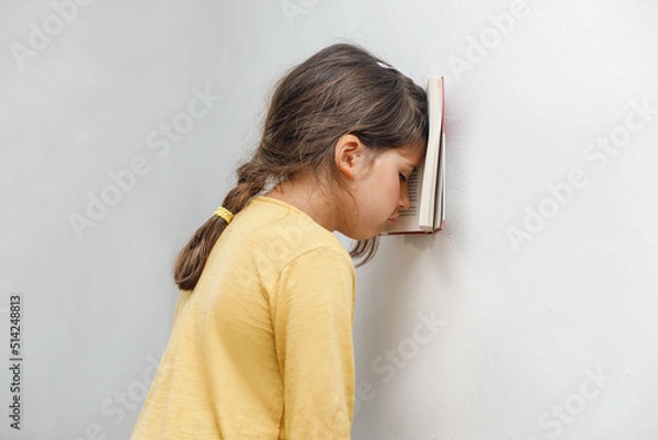 Fototapeta Sad and tired caucasian girl with dyslexia holds a wall. The child learns to speak and read correctly
