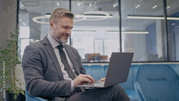 Fototapeta Successful businessman working on laptop, sitting in comfortable office and smiling