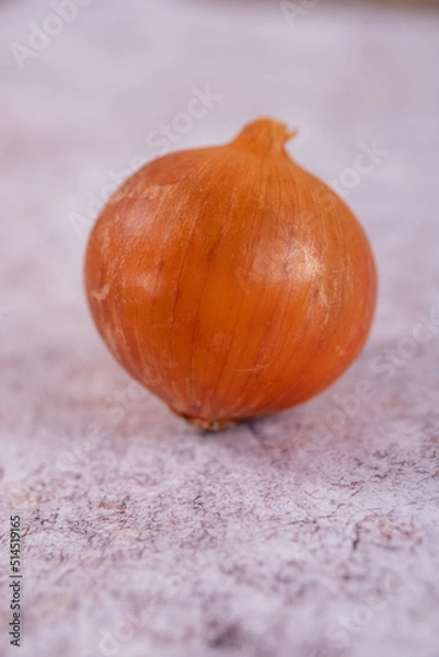 Fototapeta A whole onion on a white stone surface background.