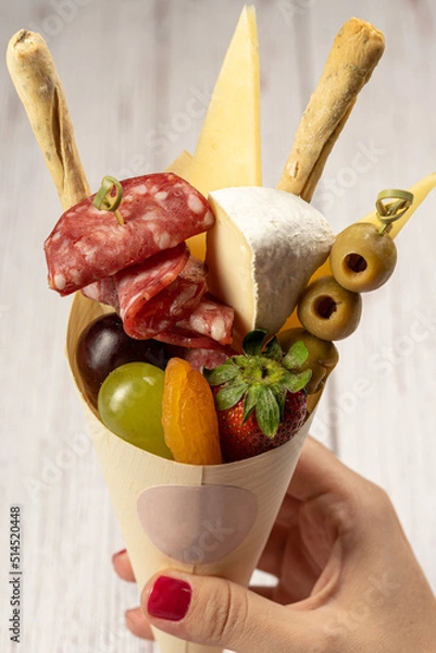 Obraz charcuterie cone with cheeses, crackers, strawberries, olives, kiwi, grapes, pastrami, salami, apricot and walnuts