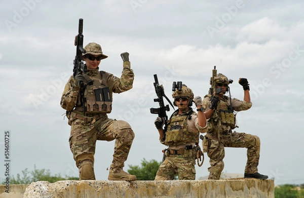 Fototapeta group of military soldier team in uniform with armforce in battle field standing on concrete bunker firing machine gun and show victory hand
