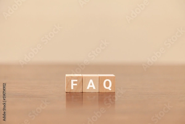 Obraz FAQの文字。よくある質問。Frequently Asked Questions。3つの木製ブロックに書かれている。白い文字。木製テーブルと白い壁紙の背景。