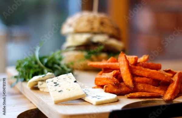 Obraz Burger w artystycznej kompozycji z frytkami i batatami oraz cebulą pieczarkami. Burgerownia - zdjęcie świeżego, apetycznego burgera