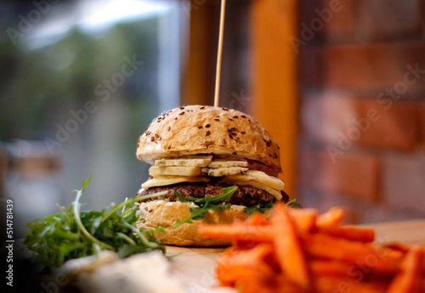 Obraz Burger w artystycznej kompozycji z frytkami i batatami oraz cebulą pieczarkami. Burgerownia - zdjęcie świeżego, apetycznego burgera
