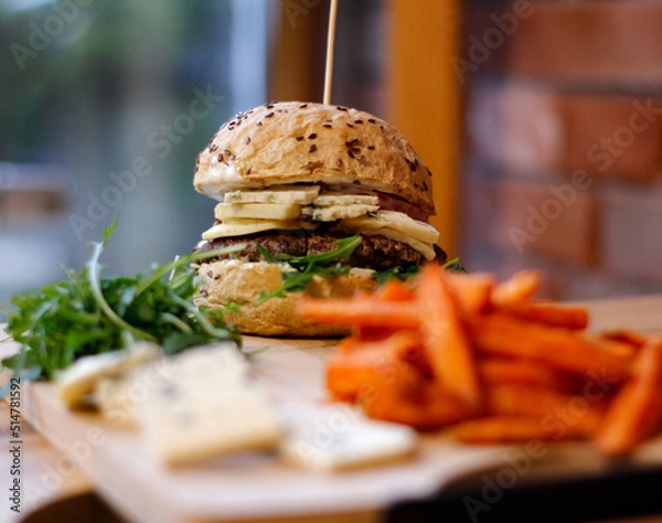 Obraz Burger w artystycznej kompozycji z frytkami i batatami oraz cebulą pieczarkami. Burgerownia - zdjęcie świeżego, apetycznego burgera