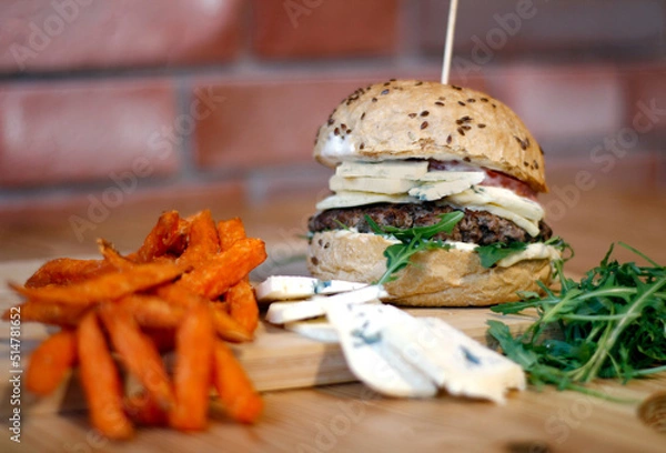 Obraz Burger w artystycznej kompozycji z frytkami i batatami oraz cebulą pieczarkami. Burgerownia - zdjęcie świeżego, apetycznego burgera