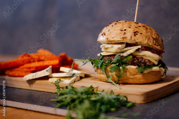 Obraz Burger w artystycznej kompozycji z frytkami i batatami oraz cebulą pieczarkami. Burgerownia - zdjęcie świeżego, apetycznego burgera