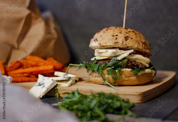 Obraz Burger w artystycznej kompozycji z frytkami i batatami oraz cebulą pieczarkami. Burgerownia - zdjęcie świeżego, apetycznego burgera