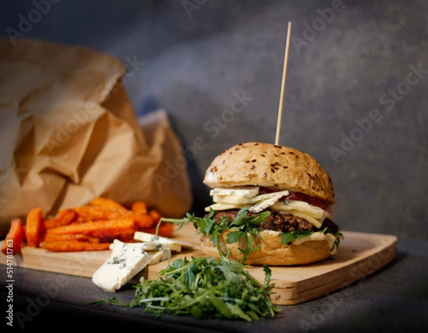 Obraz Burger w artystycznej kompozycji z frytkami i batatami oraz cebulą pieczarkami. Burgerownia - zdjęcie świeżego, apetycznego burgera