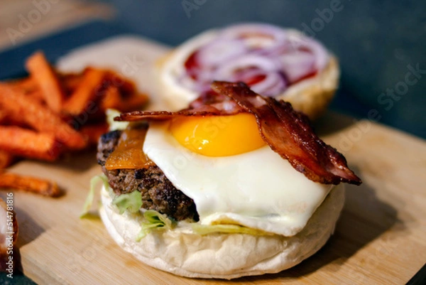 Obraz Burger w artystycznej kompozycji z frytkami i batatami oraz cebulą pieczarkami. Burgerownia - zdjęcie świeżego, apetycznego burgera