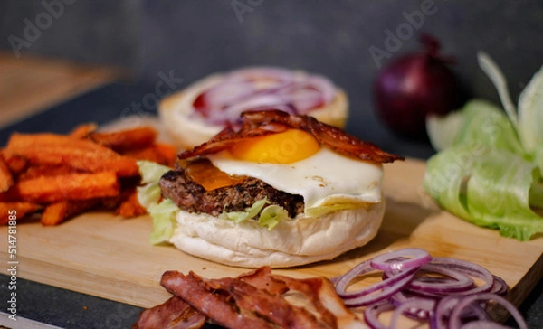 Obraz Burger w artystycznej kompozycji z frytkami i batatami oraz cebulą pieczarkami. Burgerownia - zdjęcie świeżego, apetycznego burgera
