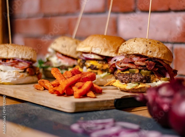 Obraz Burger w artystycznej kompozycji z frytkami i batatami oraz cebulą pieczarkami. Burgerownia - zdjęcie świeżego, apetycznego burgera