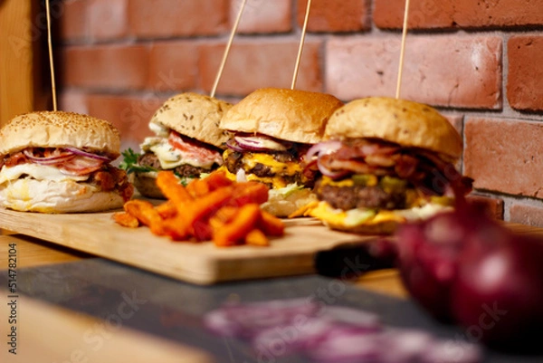 Obraz Burger w artystycznej kompozycji z frytkami i batatami oraz cebulą pieczarkami. Burgerownia - zdjęcie świeżego, apetycznego burgera