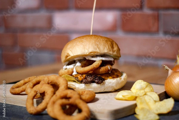 Obraz Burger w artystycznej kompozycji z frytkami i batatami oraz cebulą pieczarkami. Burgerownia - zdjęcie świeżego, apetycznego burgera