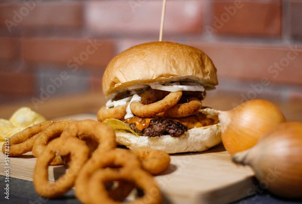 Obraz Burger w artystycznej kompozycji z frytkami i batatami oraz cebulą pieczarkami. Burgerownia - zdjęcie świeżego, apetycznego burgera