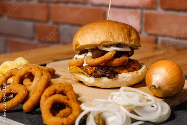 Obraz Burger w artystycznej kompozycji z frytkami i batatami oraz cebulą pieczarkami. Burgerownia - zdjęcie świeżego, apetycznego burgera