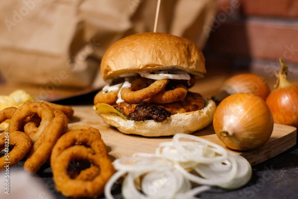 Obraz Burger w artystycznej kompozycji z frytkami i batatami oraz cebulą pieczarkami. Burgerownia - zdjęcie świeżego, apetycznego burgera